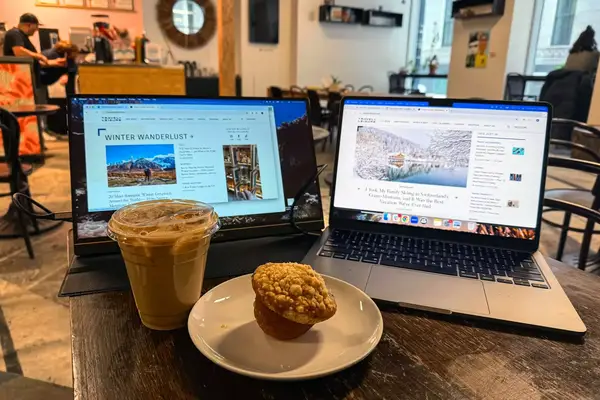 Opened ARZOPA Portable Monitor next to an opened macbook pro with a coffee and muffin in front.
