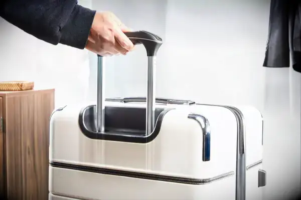 A hand holds the handle of a Travelpro x Travel & Lanetrek Carry-On Spinner