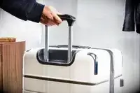A hand holds the handle of a Travelpro x Travel & Lanetrek Carry-On Spinner