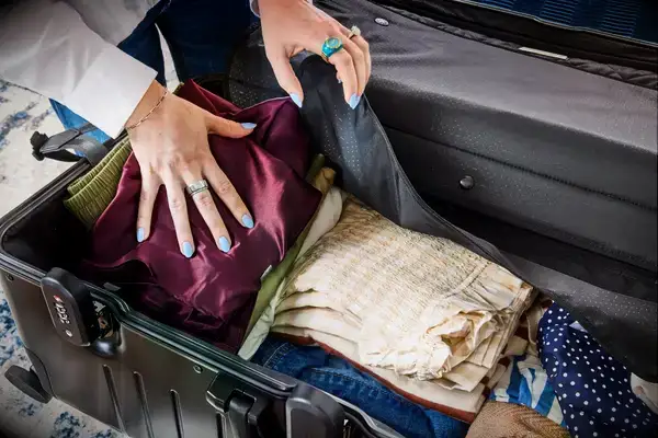 A person places folded clothing into the Monos Aluminum Trunk