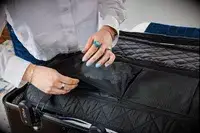 A person zips a pocket on the Monos Aluminum Trunk closed