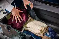 A person places folded clothing into the Monos Aluminum Trunk