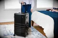 A person wheels the Monos Aluminum Trunk over a rug