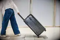 A person wheels the Monos Aluminum Trunk over stone pavers