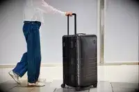 A person wheels the Monos Aluminum Trunk over stone pavers