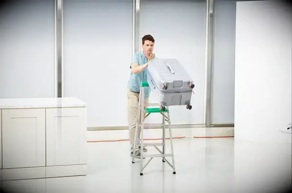 A person pushing the Delsey Paris Cruise 3.0 26 Inch Trunk off of a ladder