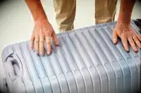 Two hands pushing the Delsey Paris Cruise 3.0 26 Inch Trunk closed