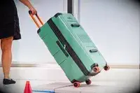 A person pulls the Delsey X Jeep JH002B Large Expandable Spinner Trunk over stone pavers