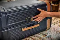 A person presses the lock on the side of the Hartmann Reserve Medium Expandable Trunk