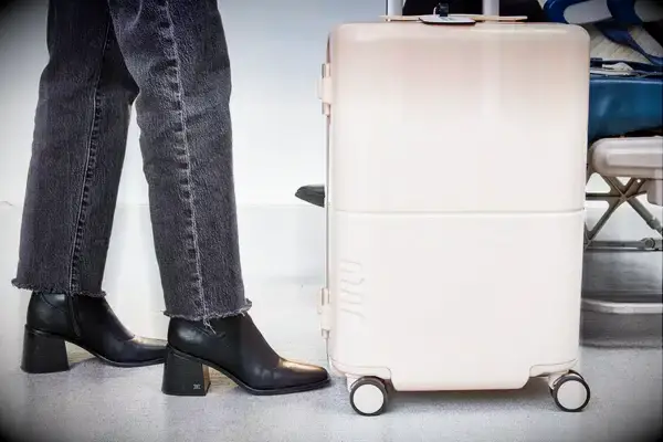 Legs and feet next to July Carry On Trunk with airplane seat in background