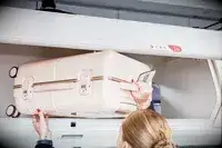 Hands putting July Carry On Trunk in the overhead bin of an airplane
