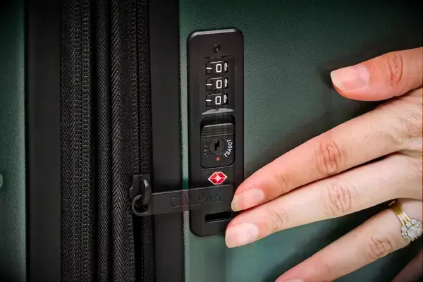 A person touches the lock on the Calpak Hue Trunk Luggage