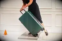 A person wheels the Calpak Hue Trunk Luggage over stone