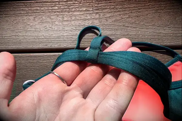 Hand holding a green fabric strap, resting on a wooden surface in sunlight