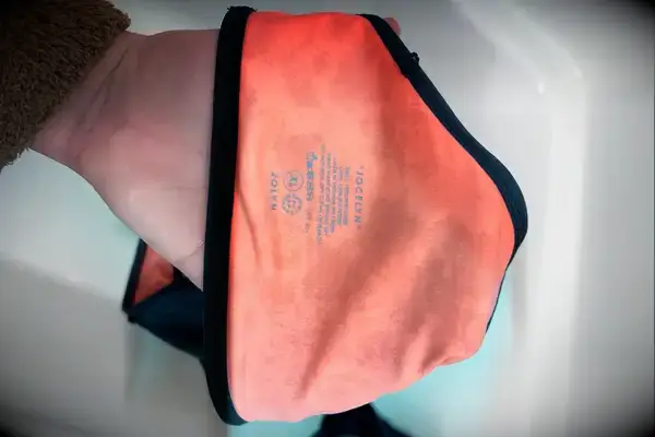 A hand holding an orange swimwear item with the brand name 