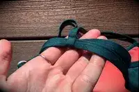 Hand holding a green fabric strap, resting on a wooden surface in sunlight