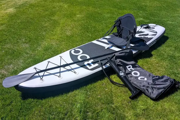 A person standing on the SereneLife Inflatable Stand-up Paddleboard while in a lake
