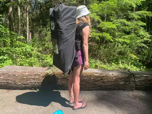 A person carrying a deflated SereneLife Inflatable Stand-up Paddleboard in its carrier 