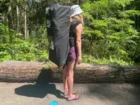 A person carrying a deflated SereneLife Inflatable Stand-up Paddleboard in its carrier 