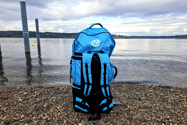The Hydrus Paradise Touring Inflatable Paddle Board in its travel bag standing by the water