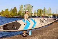 A person holding the Hydrus Paradise Touring Inflatable Paddle Board while standing outside of the water