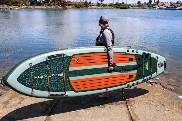 A person looking at the water while holding the iRocker BLACKFIN MODEL Inflatable Paddle Board