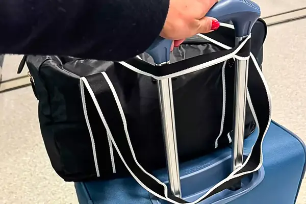 Paravel Fold-Up Bag sits on top of a blue suitcase, while a hand holds the suitcase handle