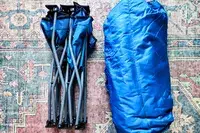 The Regalo My Cot Deluxe Portable Toddler Bed and sleeping bag folded up on a rug