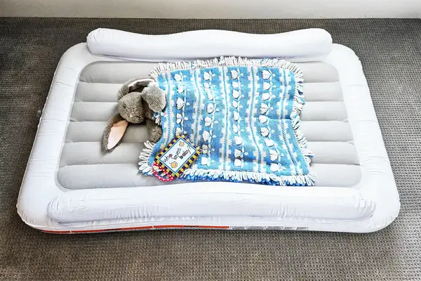 A stuffed bunny under a blanket sits on the Regalo Inflatable Toddler Bed