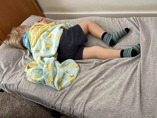 A child sleeps on the Regalo My Cot Deluxe Portable Toddler Bed