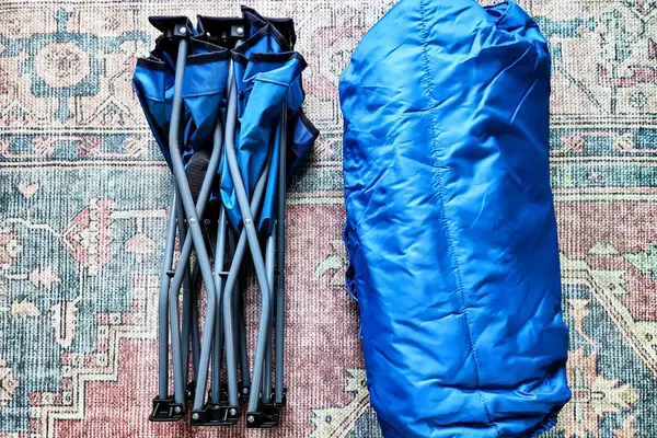 The Regalo My Cot Deluxe Portable Toddler Bed and sleeping bag folded up on a rug