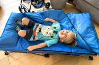 A child lies on the Regalo My Cot Deluxe Portable Toddler Bed