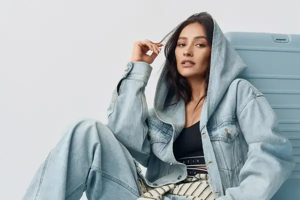 Shay Mitchell wearing a denim ensemble seated against a suitcase
