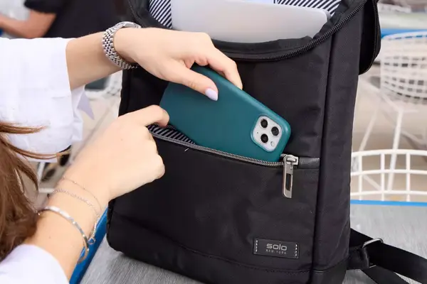 A person places a cell phone into the Solo NY Stealth Hybrid Backpack