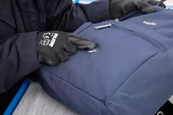 A person touches a rip in the fabric of the Baggallini Securtex Anti-Theft Vacation Backpack