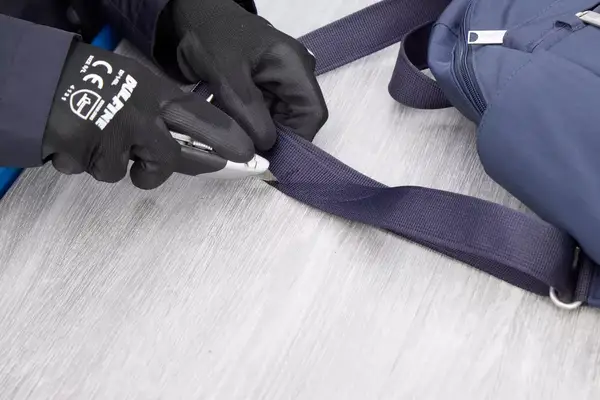 A person cuts the Baggallini Securtex Anti-Theft Vacation Backpack strap with a box cutter