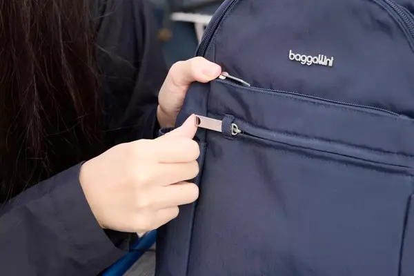 A person zips the Baggallini Securtex Anti-Theft Vacation Backpack closed