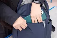 A person places a cell phone into the Baggallini Securtex Anti-Theft Vacation Backpack pocket