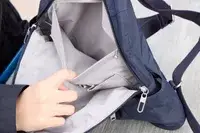 A person holds the Baggallini Securtex Anti-Theft Vacation Backpack pocket open