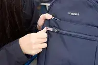 A person zips the Baggallini Securtex Anti-Theft Vacation Backpack closed