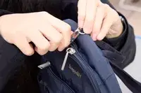 A person unzips the Baggallini Securtex Anti-Theft Vacation Backpack