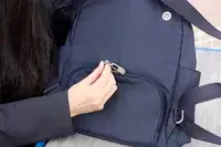 A person unzips the Baggallini Securtex Anti-Theft Vacation Backpack