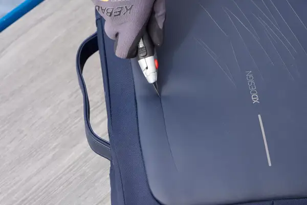 A person uses a box cutter to cut the XDDesign Bobby Bizz 3-in-1 Anti-Theft Backpack & Briefcase