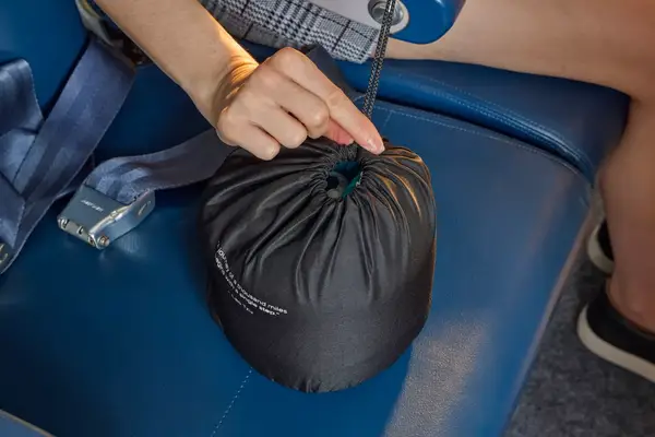 A person holding the Ostrich Pillow Go Neck Pillow in its travel pouch