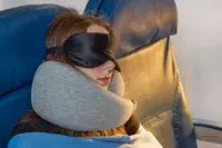 A person resting on a plane while wearing the Ostrich Pillow Go Neck Pillow