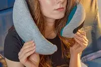 A person putting on the Ostrich Pillow Go Neck Pillow