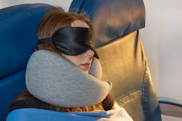 A person resting on a plane while wearing the Ostrich Pillow Go Neck Pillow