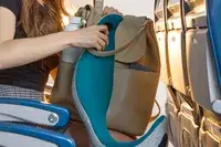 A person grabbing the Ostrich Pillow Go Neck Pillow from their bag