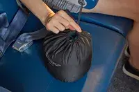 A person holding the Ostrich Pillow Go Neck Pillow in its travel pouch