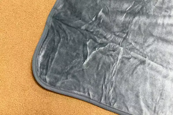 Corner of the PAVILIA Travel Blanket and Pillow displayed on a tan surface